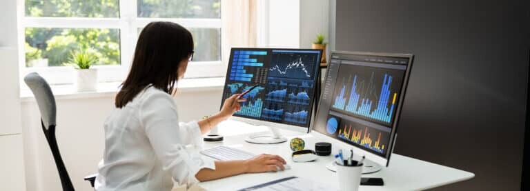 Analyst reviewing KPI data on dual monitors in a well lit office showcasing performance metrics and analytics