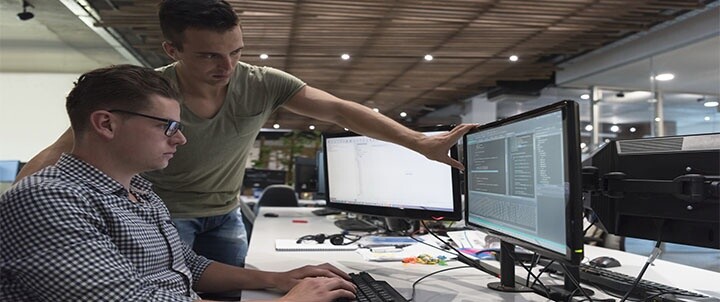 Two IT professionals collaborating at a workstation focusing on coding and problem solving to address the IT talent shortage