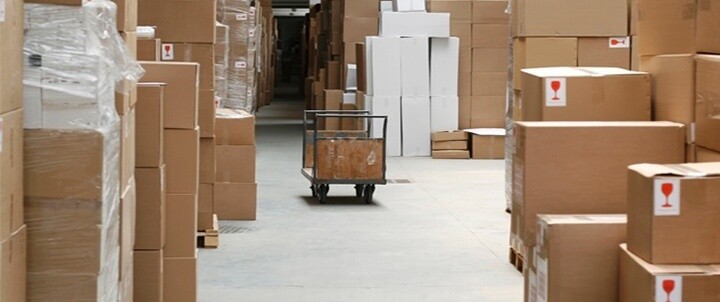Warehouse aisle filled with stacked cardboard boxes and a cart highlighting the importance of inventory management for multinationals