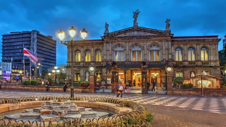 National Theatre of Costa Rica illuminated at dusk surrounded by a plaza with visitors and a fountain showcasing local architecture