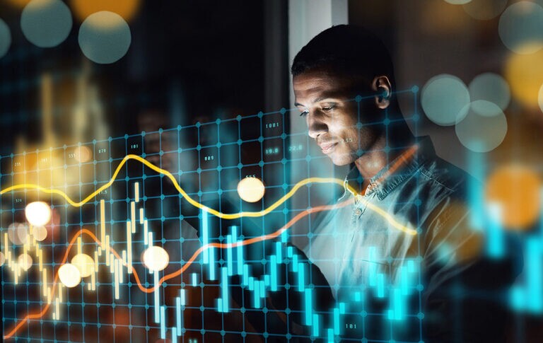 Businessman analyzing stock market data on a tablet surrounded by digital graphs and charts working late in an office setting