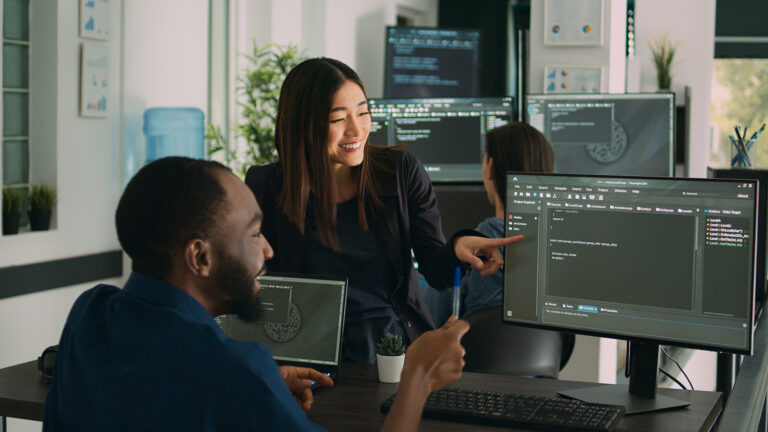 Diverse programmers celebrate a successful cloud computing project collaborating around computers and coding in a modern office setting