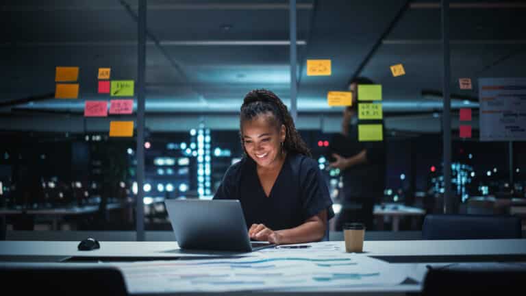 African American businesswoman working on a laptop in a city office at night managing an e commerce project with focus and enthusiasm