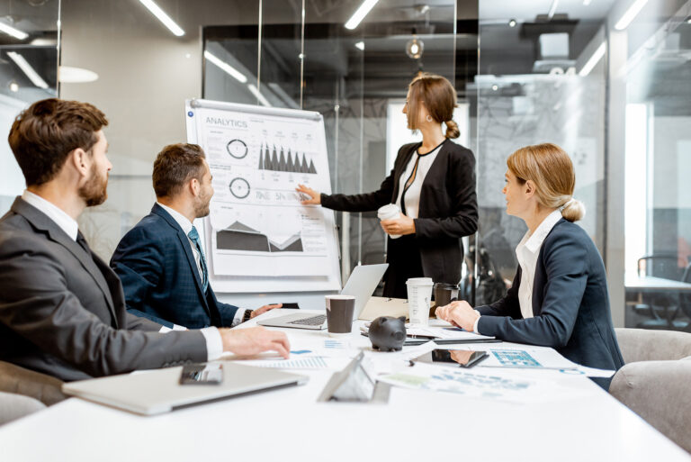 Business professionals discussing financial strategies during a conference with a presenter showing analytics on a flip chart