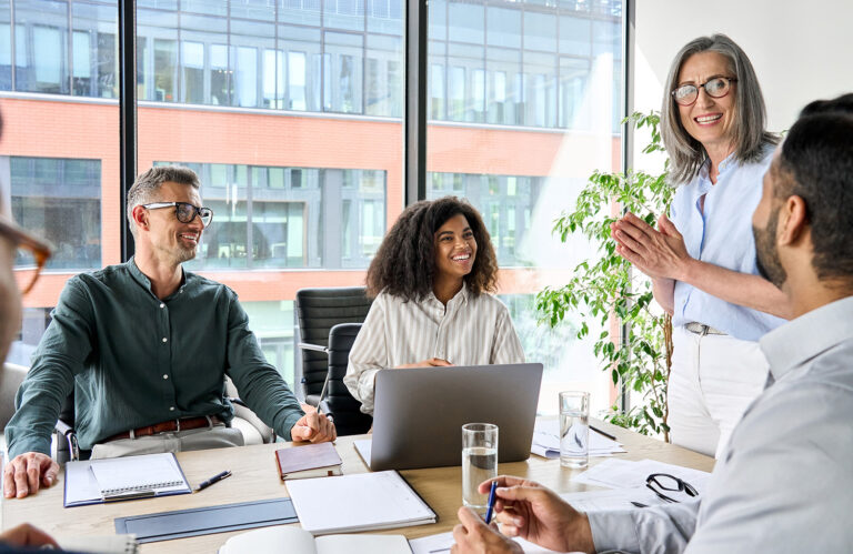 Diverse corporate team discussing project in modern boardroom featuring older female executive and engaged multicultural colleagues