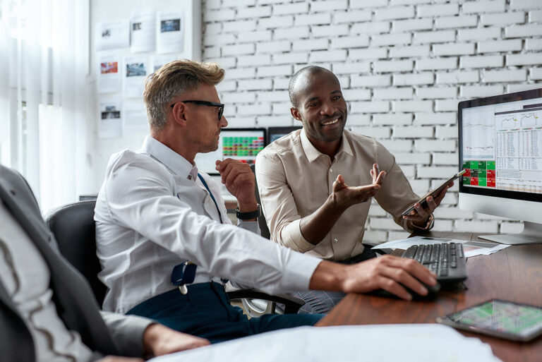 Businessmen collaborating in a modern office analyzing stock market data on computer screens illustrating finance success