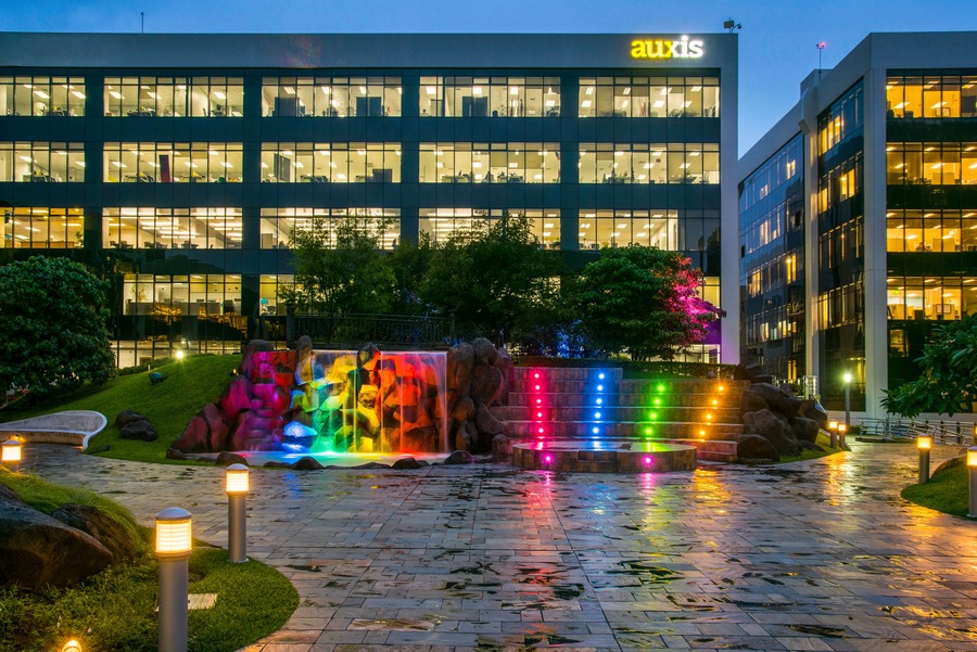Auxis office building illuminated at dusk with a colorful waterfall feature and landscaped grounds representing a modern corporate environment
