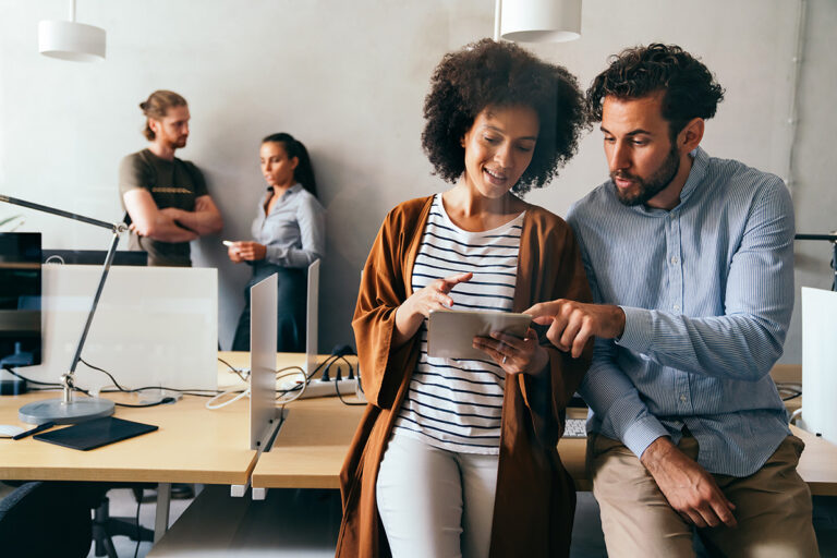 Programmers collaborating in an office discussing app development on a tablet showcasing teamwork and diversity in tech