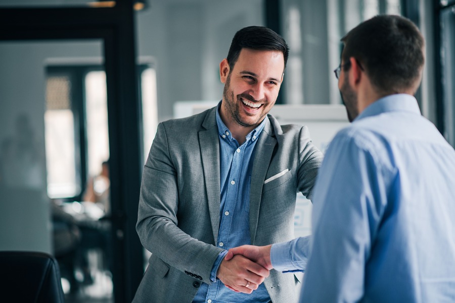 Two men shake hands in a modern office smiling and engaging positively symbolizing partnership and collaboration in business