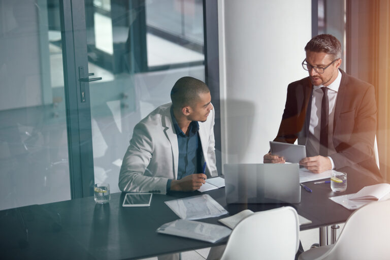 Businessman discussing finance data with a partner in a conference room using a tablet and laptop for professional planning