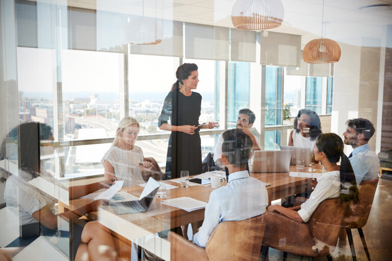 Businesswoman leads a meeting around a table engaging colleagues in a modern office with city views emphasizing collaboration and strategy