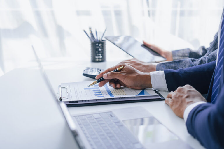 Consultant reviewing financial reports with colleagues discussing accounts payable trends and tax regulations using a tablet