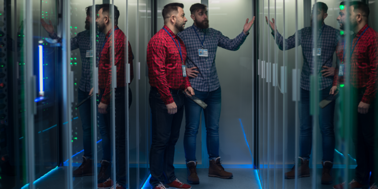 Two IT professionals discussing infrastructure management in a modern server room highlighting the benefits of outsourcing IT services