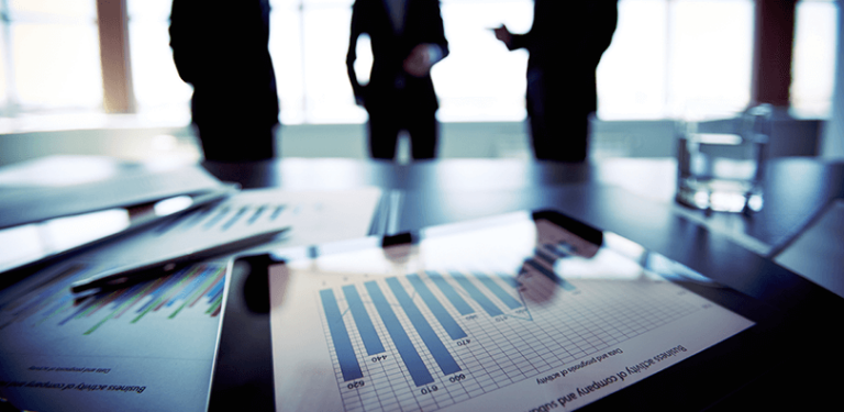 Graphs and charts on a table with business professionals discussing finance highlighting reasons for CFOs to outsource operations