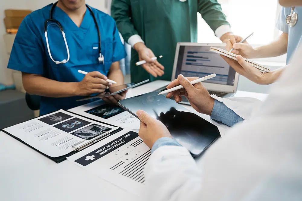 Healthcare professionals analyzing medical data and discussing X ray images on tablets and laptops
