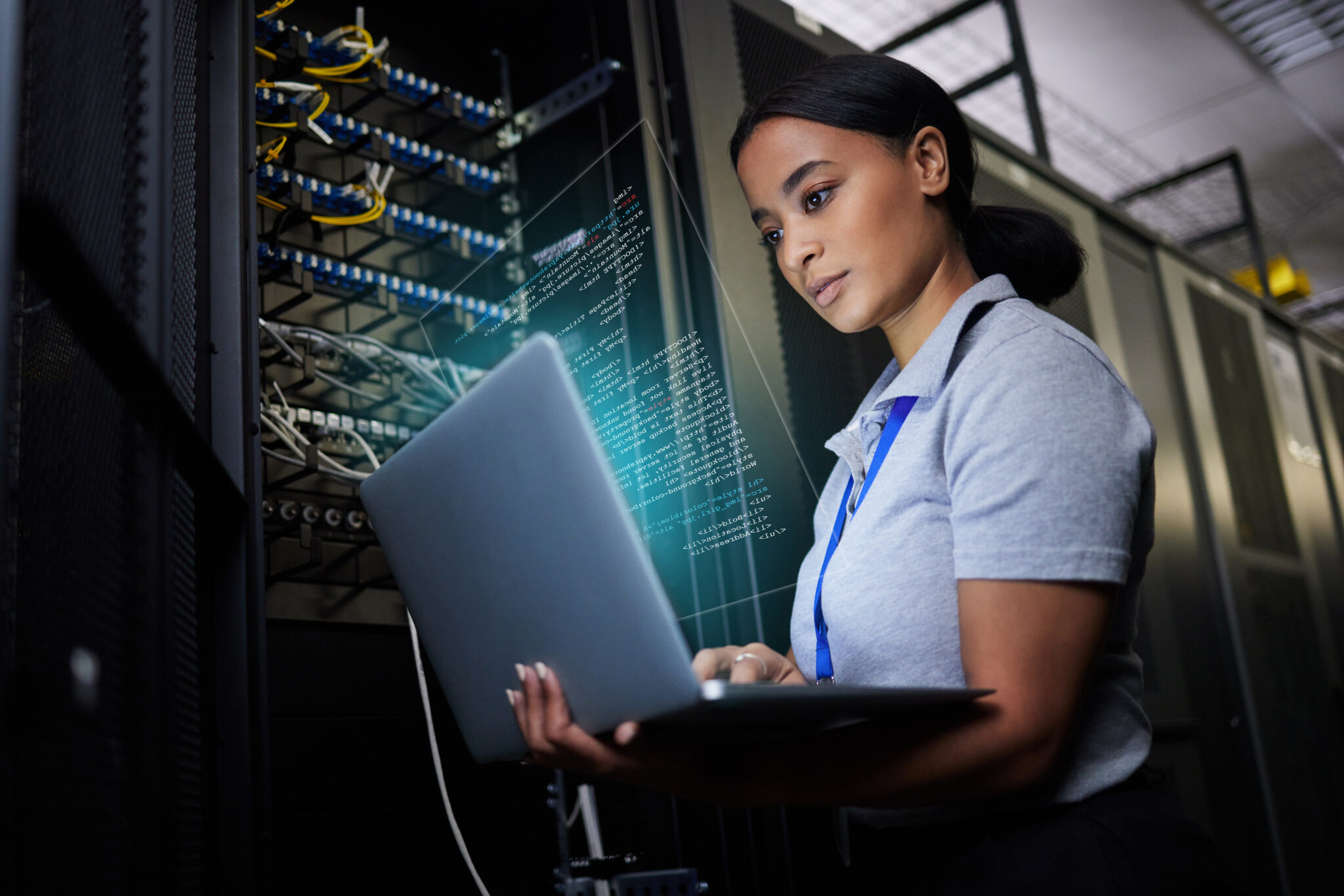 Black female IT support engineer troubleshooting in a dark server room highlighting cybersecurity and data analytics on a laptop