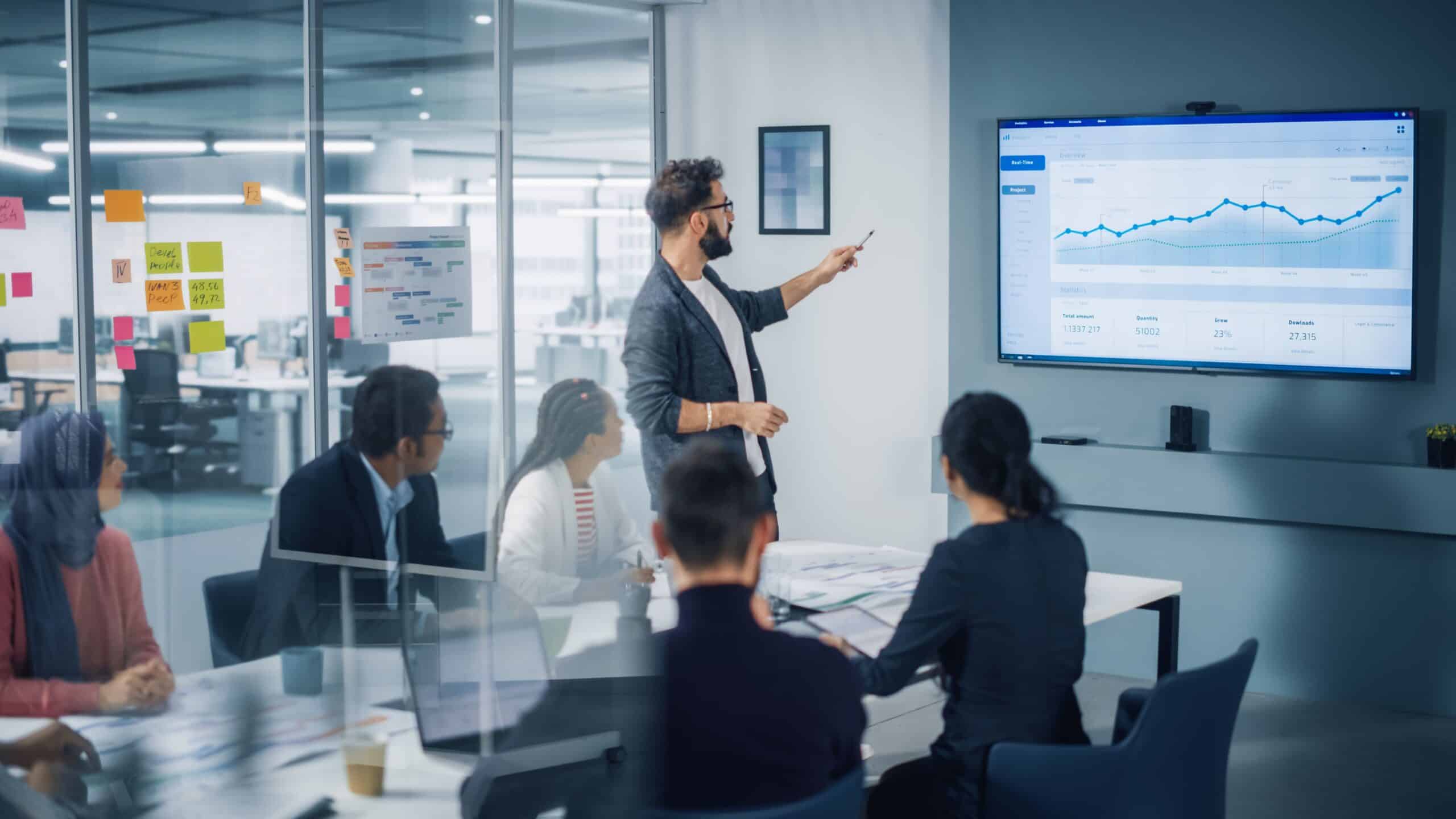A business meeting in a modern office with a presenter discussing finance transformation data displayed on a screen