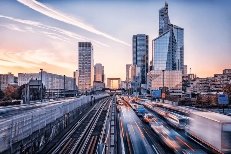 Urban skyline at sunset with busy traffic and modern buildings reflecting the vibrant city life. - Auxis Urban skyline at sunset with busy traffic and modern buildings reflecting the vibrant city life