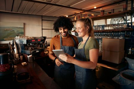 Two people in an artisanal coffee shop using a tablet reviewing business data and collaborating in a friendly environment