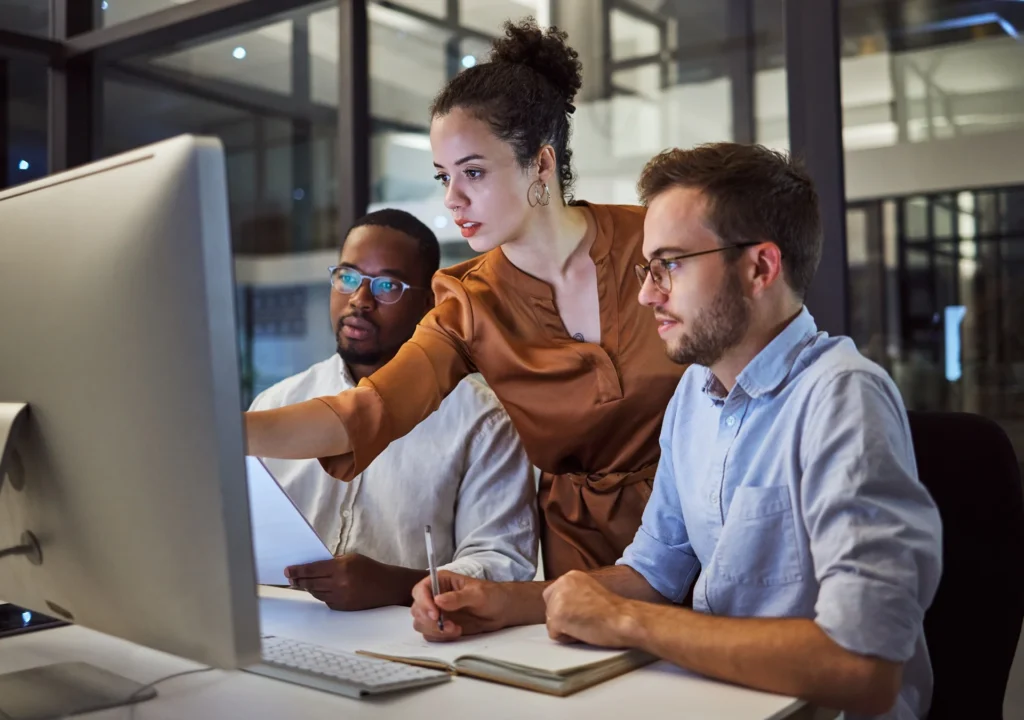 Collaborative team discussing a project at a modern workspace focusing on a computer screen with documents in hand