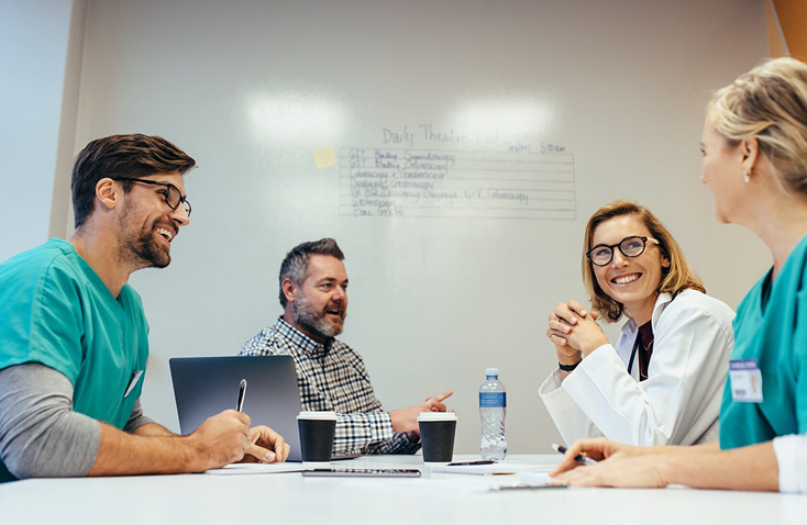Healthcare team collaborating in a meeting discussing daily themes with laptops and coffee cups on the table