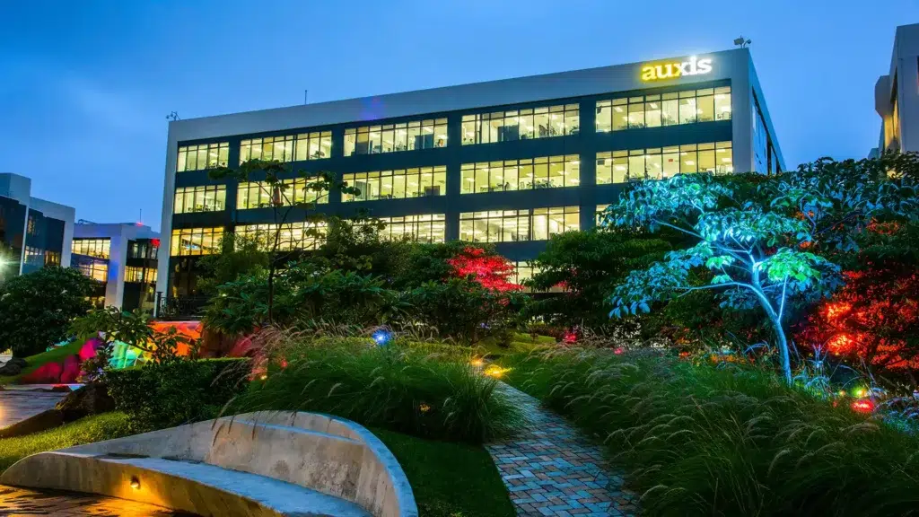 Modern office building surrounded by lush greenery and colorful lighting showcasing Auxis vibrant work environment