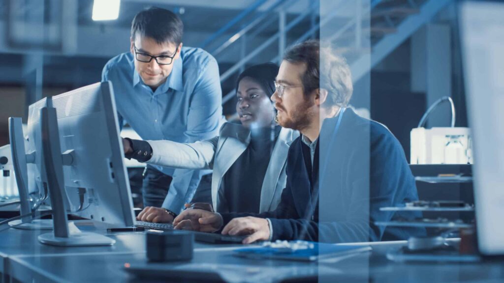 Three professionals collaborating at a computer discussing automation solutions in a modern office environment