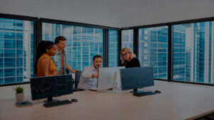 A diverse team collaborates around monitors displaying financial data strategizing in a modern office setting