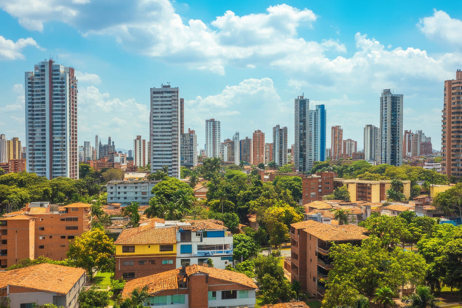 Urban skyline featuring modern high-rises and lush greenery, showcasing a vibrant city landscape under a bright blue sky.