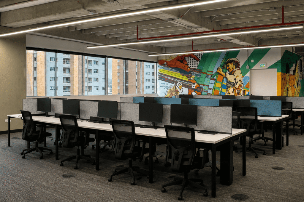 Modern office space featuring workstations with computers, complemented by a vibrant mural and large windows.