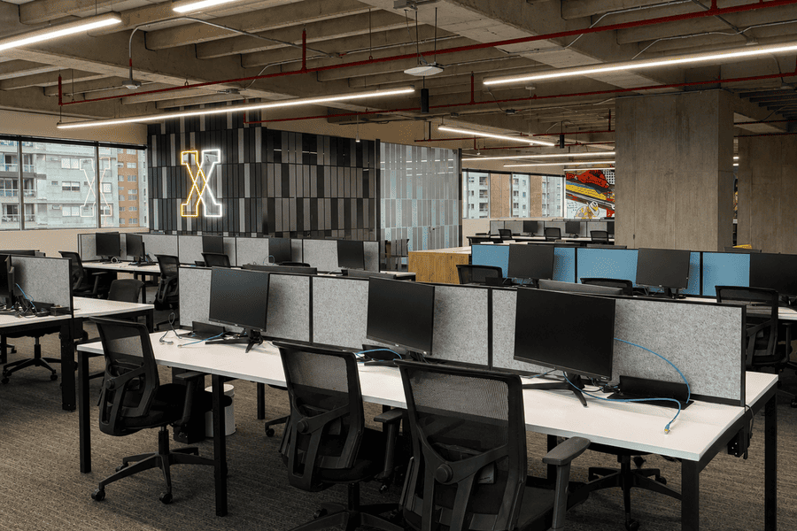Modern office space featuring rows of desks with multiple computer monitors, designed for collaborative work.