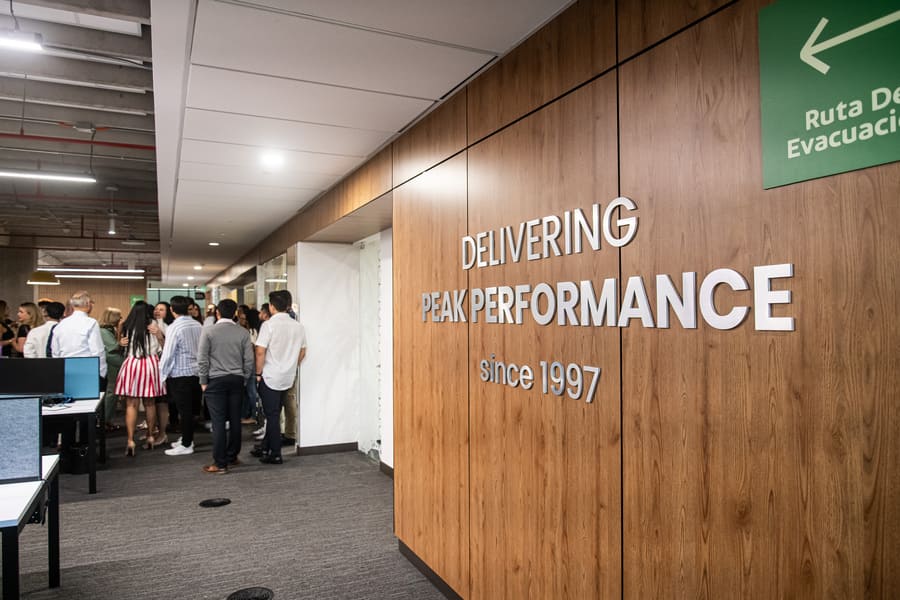 Modern office space featuring a crowd engaged in conversation, highlighting the theme of delivering peak performance.