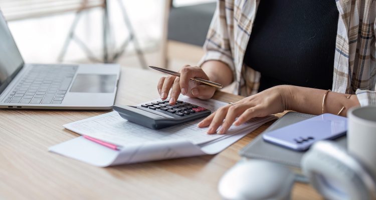 Young asian female work with financial papers at home count on calculator before paying taxes receipts online by phone. Millennial woman planning budget glad to find chance for economy saving money.