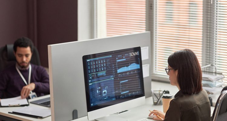 High angle view of two office workers at desk with partition wall, focus on data on computer screen