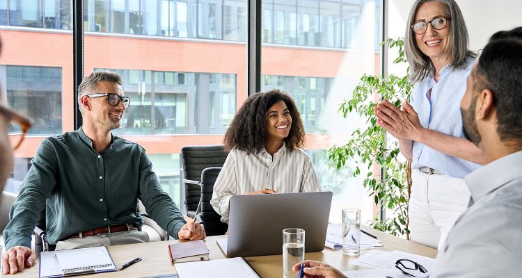 Senior older female executive ceo and happy multicultural business people discuss corporate project at boardroom table. Smiling diverse corporate team working together in modern meeting room office.