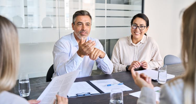 Diverse professional executive team working at meeting in office. Mid aged business man manager leader talking to board people consulting partners investors discussing project management in teamwork.