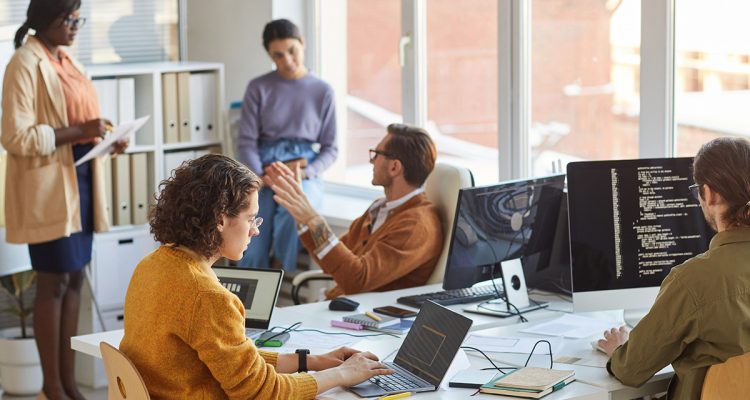 Diverse team of young software programmers using computers and writing code while collaborating on project in IT development studio, copy space