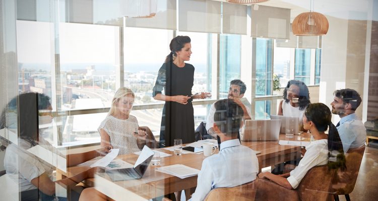 Businesswoman Leads Meeting Around Table Shot Through Door