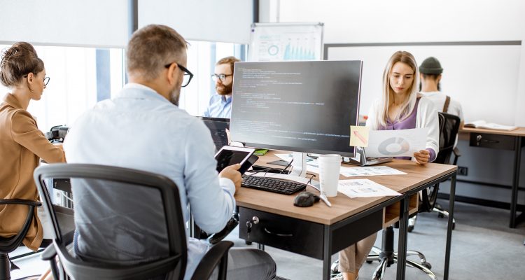 Group of diverse colleagues working on the computers in the modern office or coworking space, writing programming code